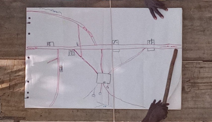 Hands point with a stick at a hand-drawn map of the areas the community uses